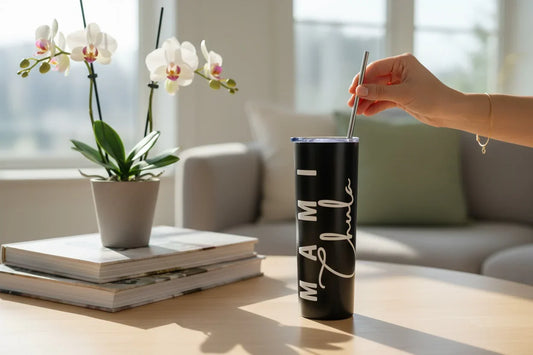 Person holding a black tumbler with 'Mami Chula' printed on it, next to a potted orchid and books on a table.