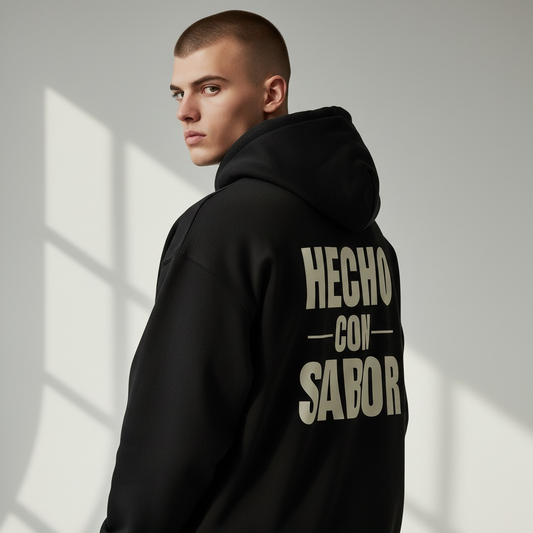 Person wearing a black hoodie with 'HECHO CON SABOR' text on the back, standing against a light gray background.